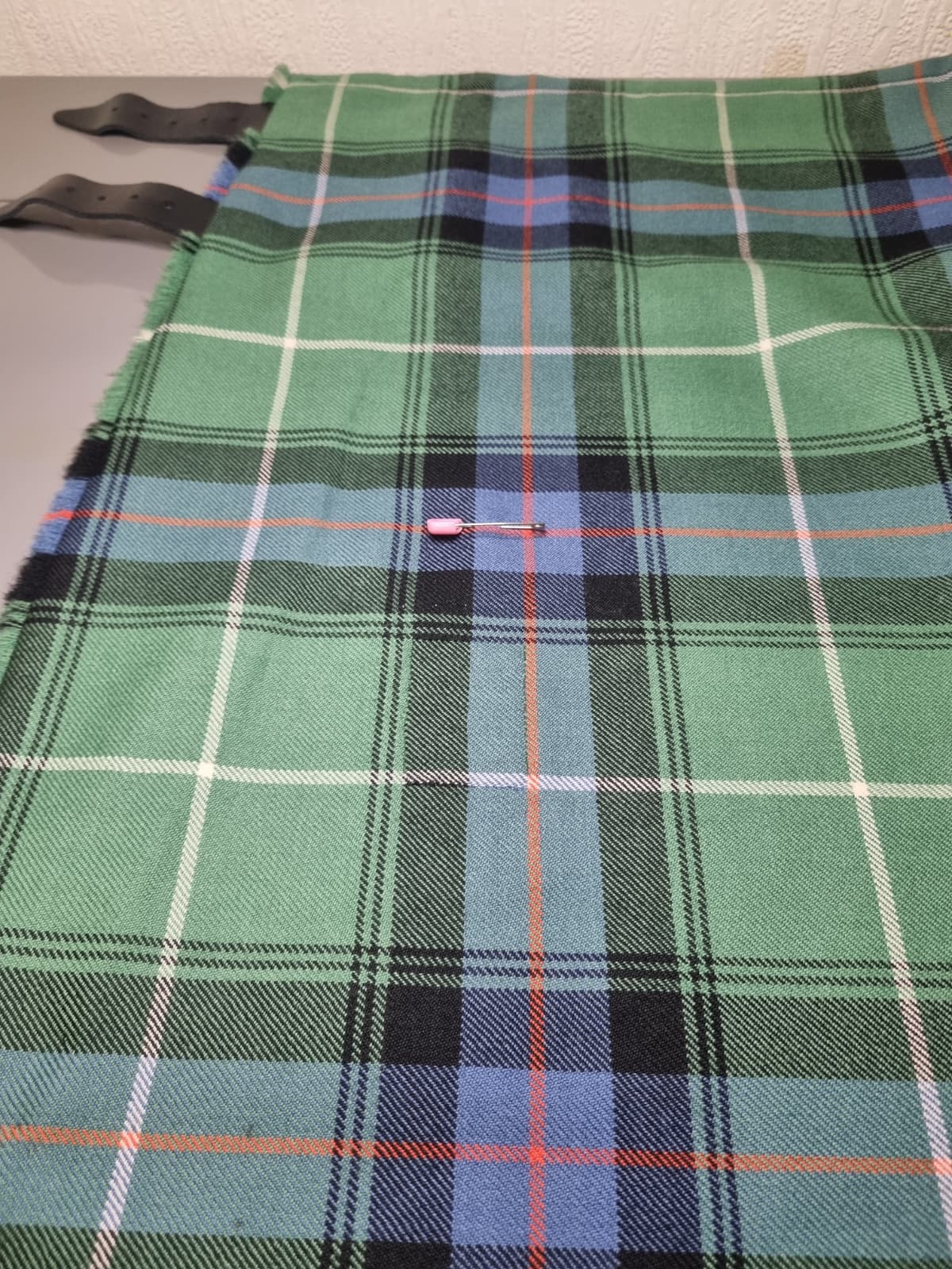 Green and blue tartan kilt fabric after targeted hole repair and pattern alignment.